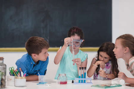 Elementary School Science Classroom: Enthusiastic Teacher Explains Chemistry to Diverse Group of Children, Little Boy Mixes Chemicals in Beakers. Children Learn with Interestの写真素材