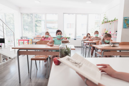Multiracial group of kids wearing face masks working at class, writing and listening explanations of...