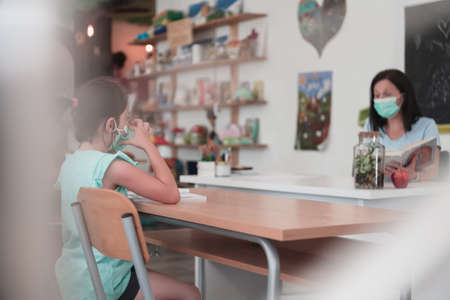 Multiracial group of kids wearing face masks working at class, writing and listening explanations of teacher in classroomの写真素材