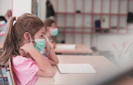 Multiracial group of kids wearing face masks working at class, writing and listening explanations of teacher in classroomの写真素材