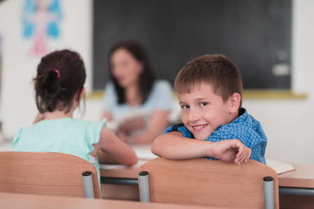 Little boy sitting in elementary school drawing on paper with their friends while sitting in a modern classroomの写真素材