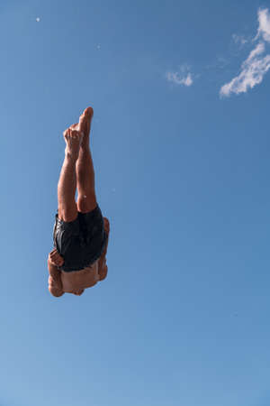 Young teen boy jumping flying and diving in the river. Clear blue sky and trees in distance as a natural background.の写真素材