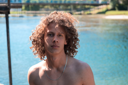 Portrait of a young teen boy with curly wet hair near the river having fun with friends at a summer...