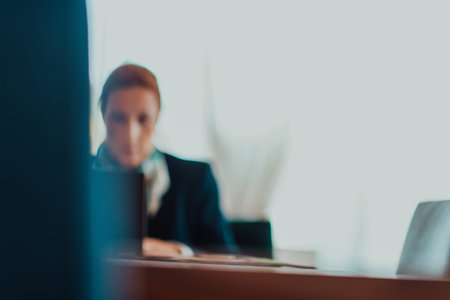 Blurred photo of an elderly woman using a laptop to carry out business projects and tasks while sitting in a modern corporationの写真素材