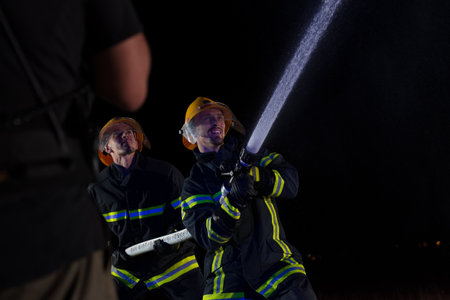 Firefighters use a water hose to eliminate a fire hazard. Team of firemen in the dangerous rescue mission.の写真素材
