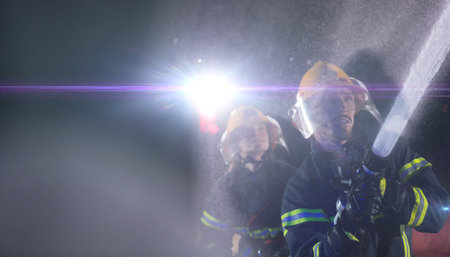 Firefighters using a water hose to eliminate a fire hazard. Team of female and male firemen in...