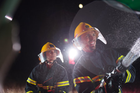 Firefighters using a water hose to eliminate a fire hazard. Team of female and male firemen in dangerous rescue mission.の写真素材