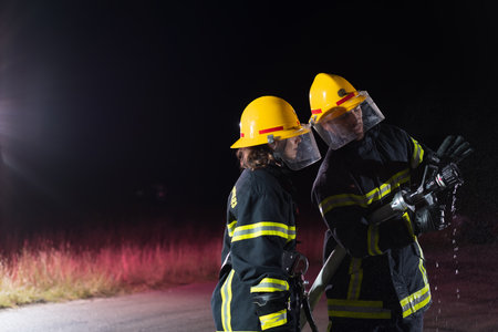 Firefighters using a water hose to eliminate a fire hazard. Team of female and male firemen in dangerous rescue mission.の写真素材