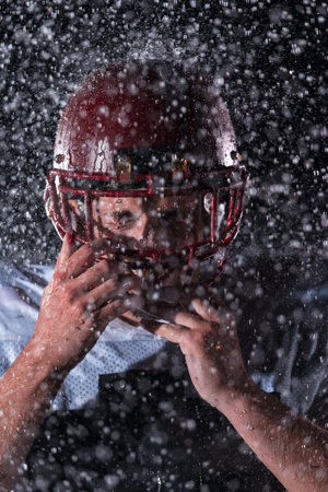 American Football Field: Lonely Athlete Warrior Standing on a Field Holds his Helmet and Ready to Play. Player Preparing to Run, Attack and Score Touchdown. Rainy Night with Dramatic Fog, Blue Lightの写真素材