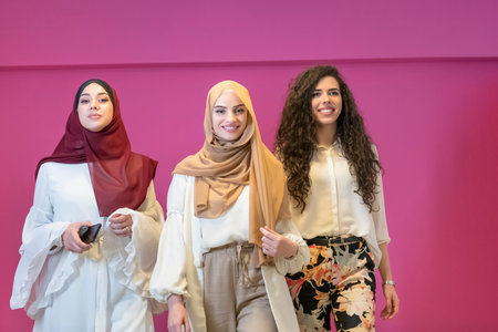 three Muslim women in hijab in a modern clothes pose against a pink background