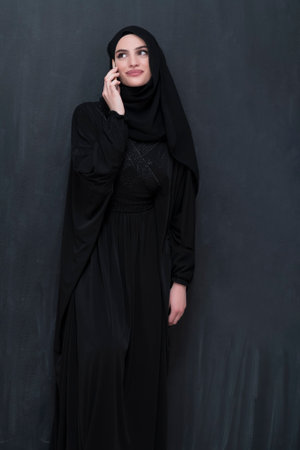 Young modern muslim business woman using smartphone wearing hijab clothes in front of black chalkboardの写真素材