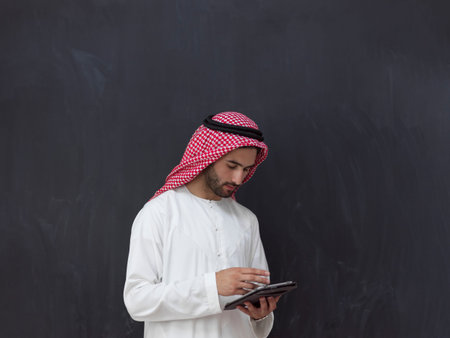 young arabian muslim businessman using tablet computer wearing hijab clothes in front of black chalkboardの写真素材