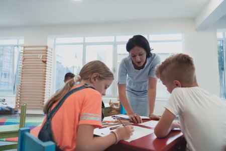 Creative kids during an art class in a daycare center or elementary school classroom drawing with female teacher.の写真素材