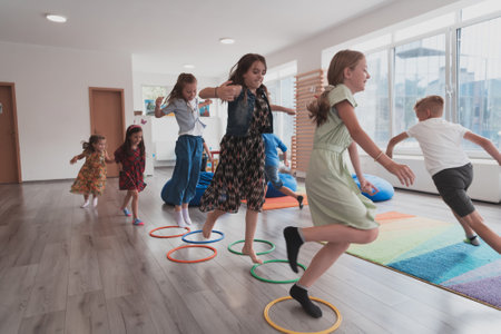 Small nursery school children with female teacher on floor indoors in classroom, doing exercise. Jumping over ring hoop circles track on the floor.の写真素材