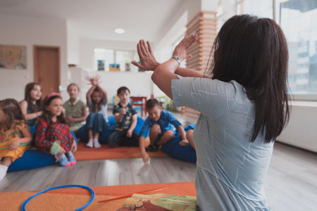 A happy female teacher sitting and playing hand games with a group of little schoolchildrenの写真素材