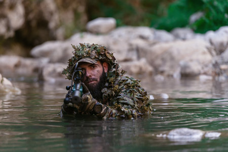 A military man or airsoft player in a camouflage suit sneaking the river and aims from a sniper rifle to the side or to target.の写真素材