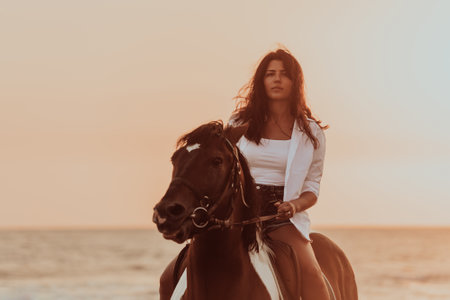 Woman in summer clothes enjoys riding a horse on a beautiful sandy beach at sunset. Selective focusの写真素材