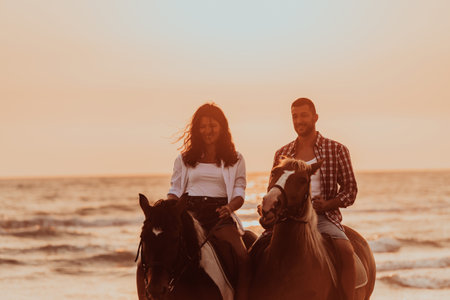 A loving couple in summer clothes riding a horse on a sandy beach at sunset. Sea and sunset in the background. Selective focusの写真素材