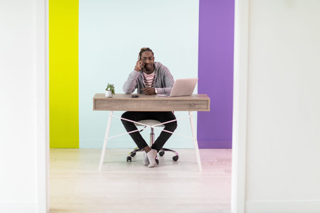 Smiling young african man freelancer using laptop and smartphone studying online working from home