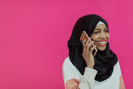 Afro woman uses a smartphone in front of a pink backgroundの写真素材