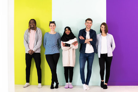 Diverse teenagers using mobile devices while posing for a studio photo in front of a colorful backgroundの写真素材