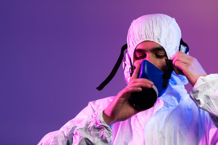 Coronavirus covid-19 pandemic. Doctor scientist wearing protective biological suit and mask due to global healthcare epidemic warning and danger background in blue and pink neon lights background.の写真素材