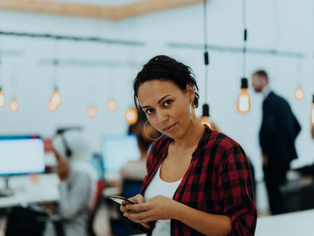 Woman sitting at workplace desk holds smartphone staring at laptop, synchronize data between...