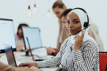 African American muslim woman with hijab and headset working as customer support in a modern office.の写真素材