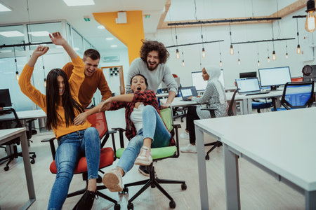 Team building and office fun. Young cheerful businesspeople in smart casual wear having fun while racing on office chairs and smiling.の写真素材