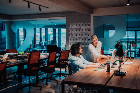 A businessman in a wheelchair in a modern coworking office space working with a female colleague late at nigh. Colleagues in the backgroundの写真素材