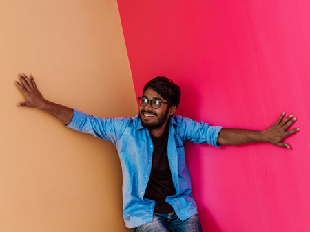 A young Indian student in a blue shirt with glasses posing on pink-orange backgroundの写真素材