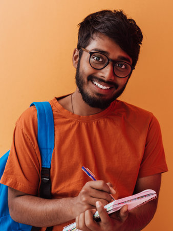 Indian student with blue backpack, glasses and notebook posing on orange background. The concept of education and schooling. Time to go back to schoolの写真素材