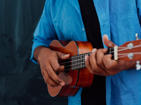 Indian young man in a blue shirt and glasses playing the guitar in front of the school blackboardの写真素材