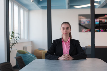 Successful young female leader in a suit with a pink shirt sitting in a modern glass office with a...