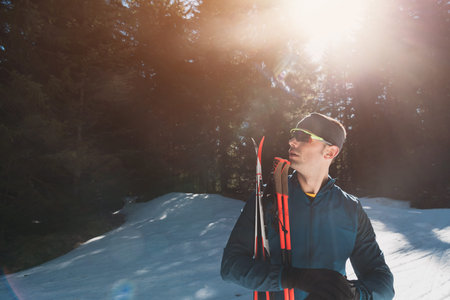 Portrait handsome male athlete with cross country skis in hands and goggles, training in snowy forest. Healthy winter lifestyle concept.の写真素材