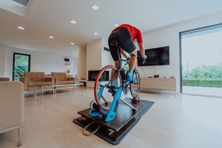 A man riding a triathlon bike on a machine simulation in a modern living room. Training during...