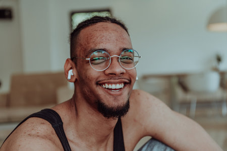Head shot of African American man wearing glasses and headphones sitting on living room floorの写真素材