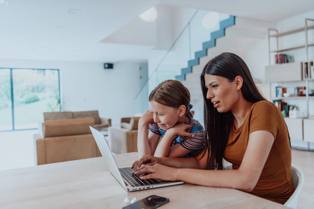 Mother with her daughter talking on laptop with family and friends while sitting in modern living room of big houseの写真素材