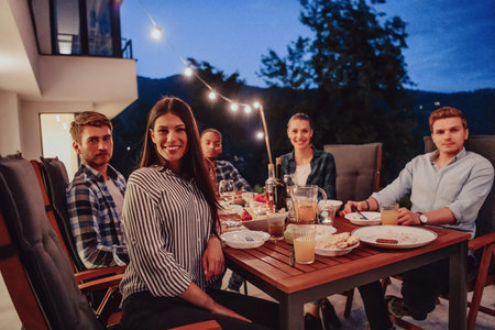 A group of young diverse people having dinner on the terrace of a modern house in the evening. Fun...