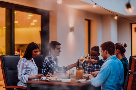 A group of young diverse people having dinner on the terrace of a modern house in the evening. Fun for friends and family. Celebration of holidays, weddings with barbecue.の写真素材