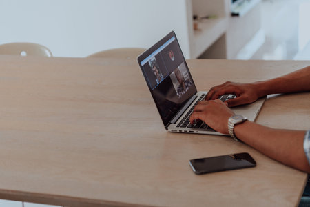 African American man in glasses sitting at a table in a modern living room, using a laptop for business video chat, conversation with friends and entertainmentの写真素材