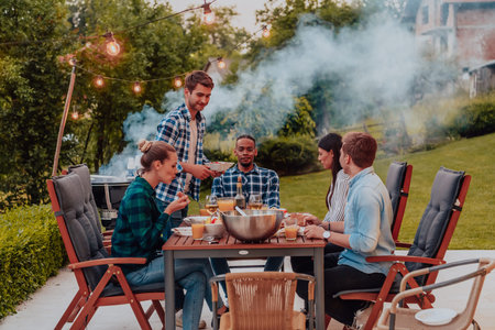 A group of young diverse people having dinner on the terrace of a modern house in the evening. Fun for friends and family. Celebration of holidays, weddings with barbecue.の写真素材
