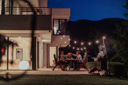 A group of young diverse people having dinner on the terrace of a modern house in the evening. Fun for friends and family. Celebration of holidays, weddings with barbecue.の写真素材