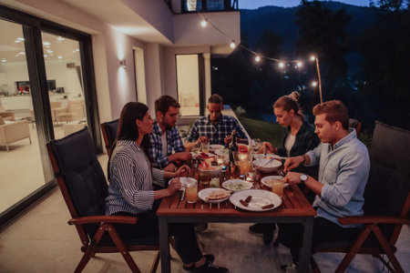 A group of young diverse people having dinner on the terrace of a modern house in the evening. Fun for friends and family. Celebration of holidays, weddings with barbecue.の写真素材