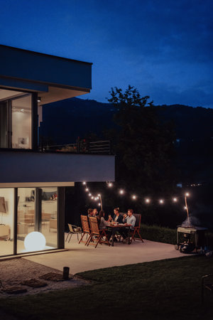 A group of young diverse people having dinner on the terrace of a modern house in the evening. Fun for friends and family. Celebration of holidays, weddings with barbecue.の写真素材