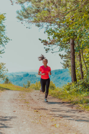 Young happy woman enjoying in a healthy lifestyle while jogging on a country road through the beautiful sunny forest, exercise and fitness conceptの写真素材