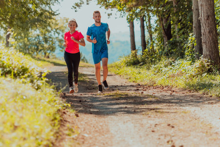 Couple enjoying in a healthy lifestyle while jogging on a country road through the beautiful sunny...