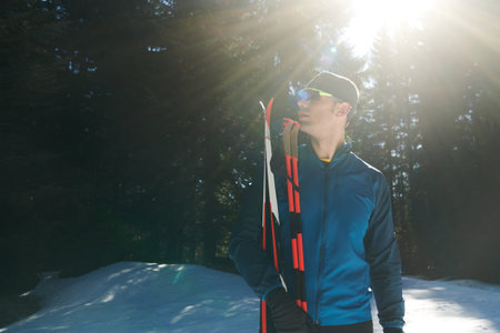 Portrait handsome male athlete with cross country skis in hands and goggles, training in snowy...