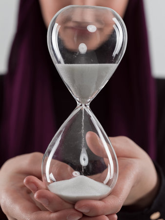 Beautiful arab businesswoman wearing hijab and holding sand clock. Time is passing and its a...