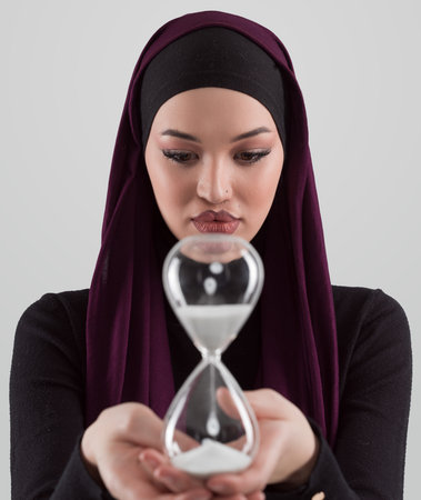 Beautiful arab businesswoman wearing hijab and holding sand clock. Time is passing and its a...